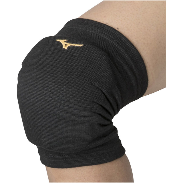 A black Mizuno knee pad worn on a person's leg, featuring the Mizuno logo in gold color on the front.